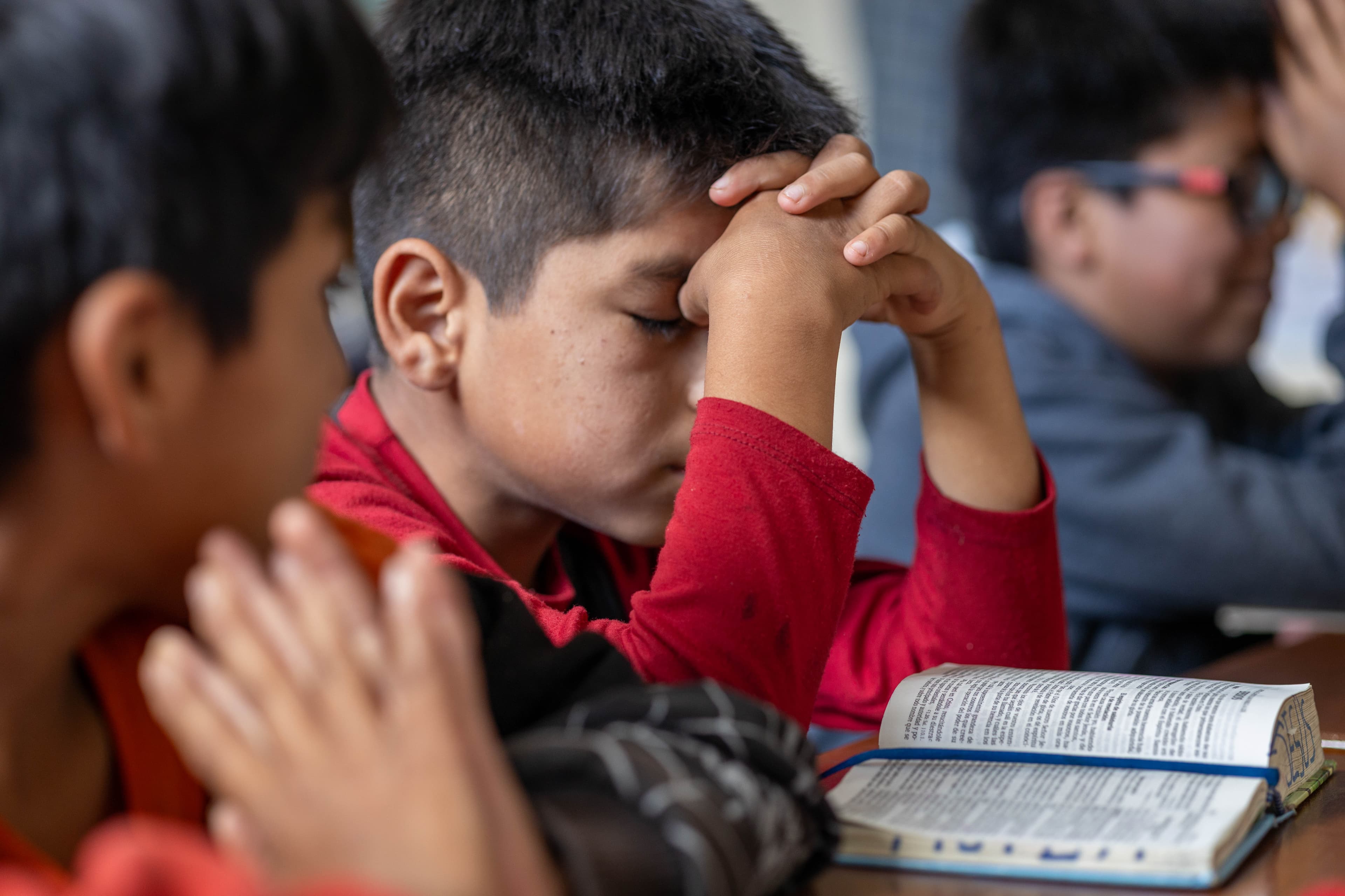 A young boy sits with his head in his hands in front of an open Bible.