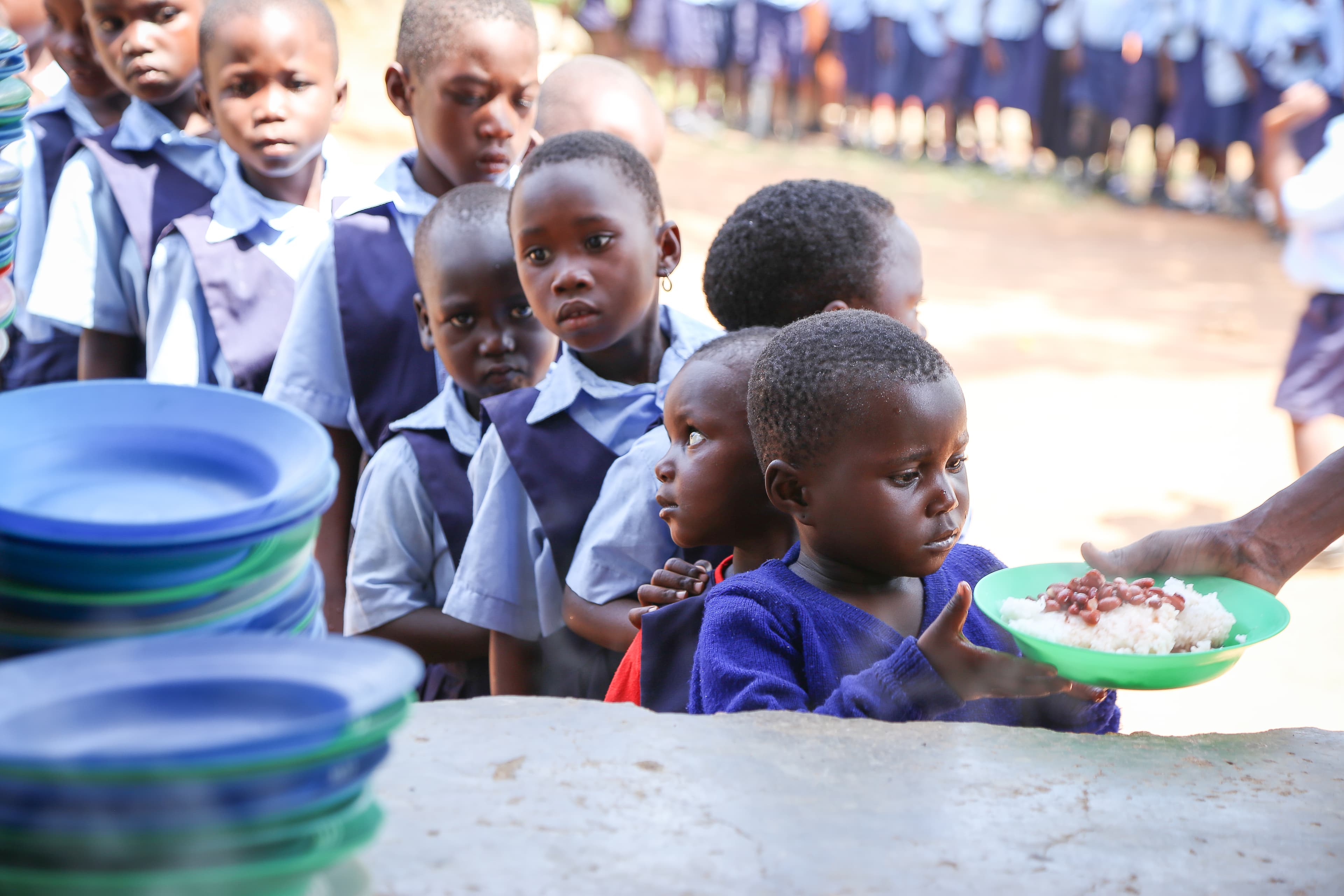 A young child is standing in line, receiving a bowl of rice and beans.