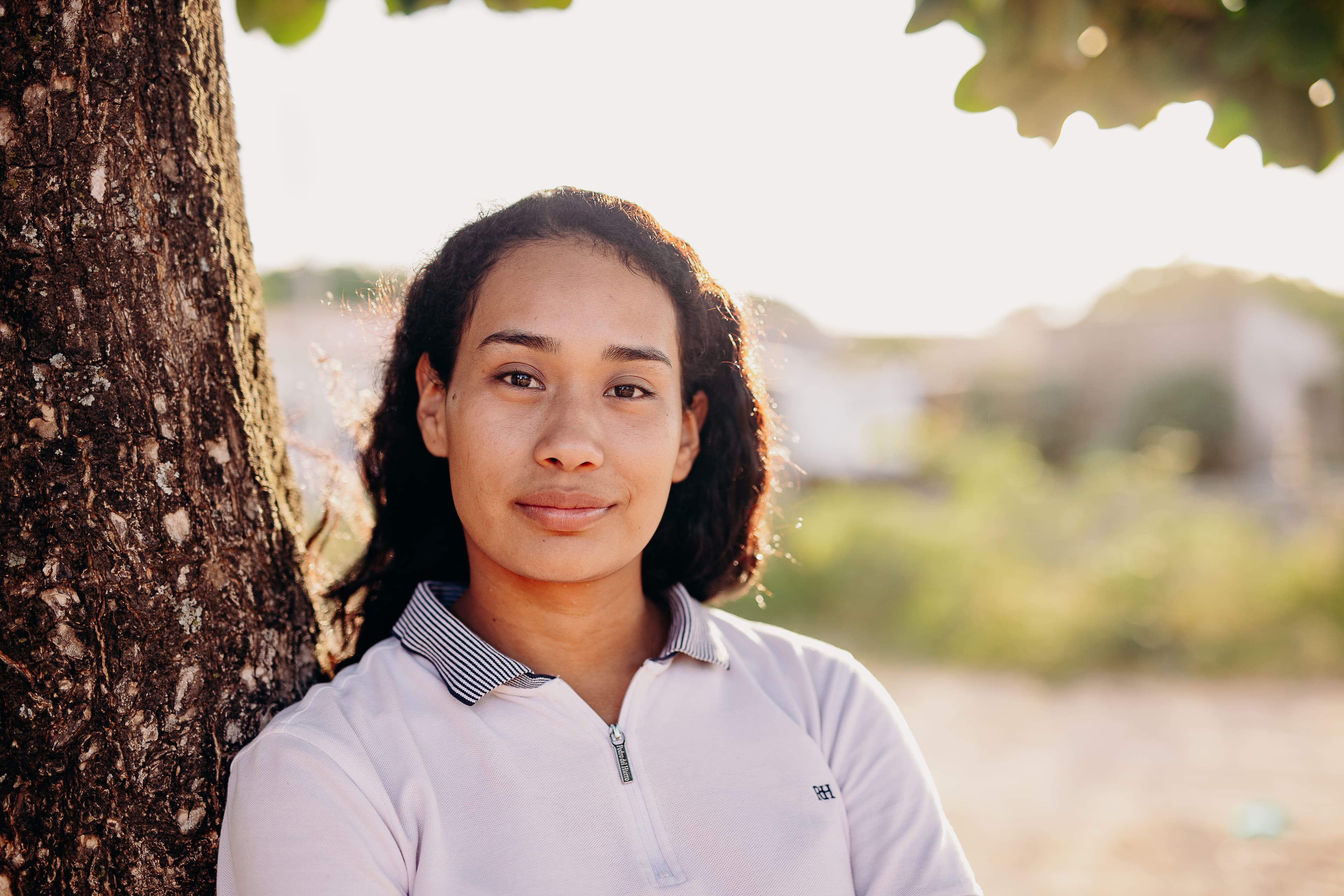 A teen Bolivian girl leans against a tree while smiling for the camera.