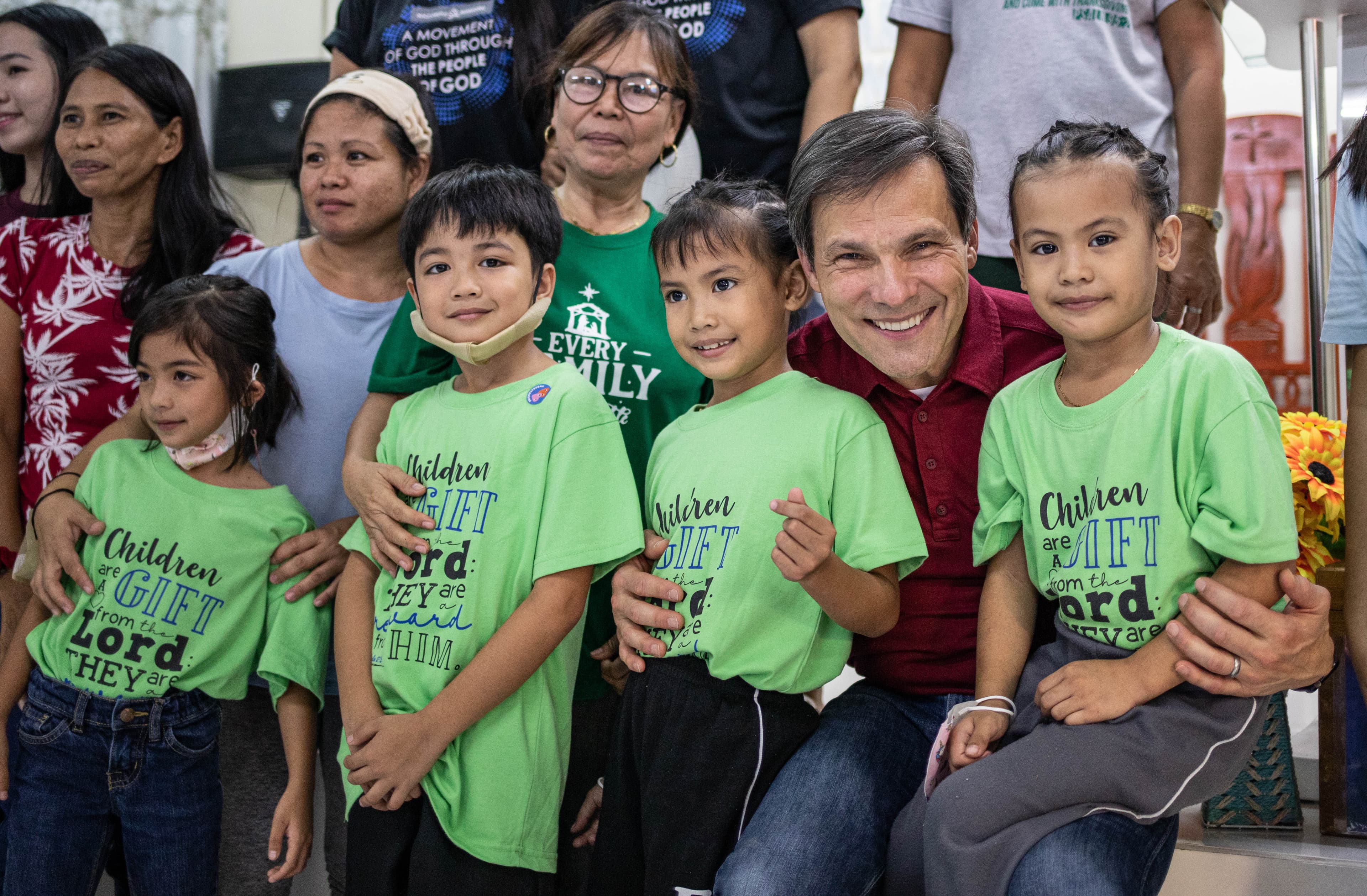 An older man stands with a group of children as they all smile for the camera.