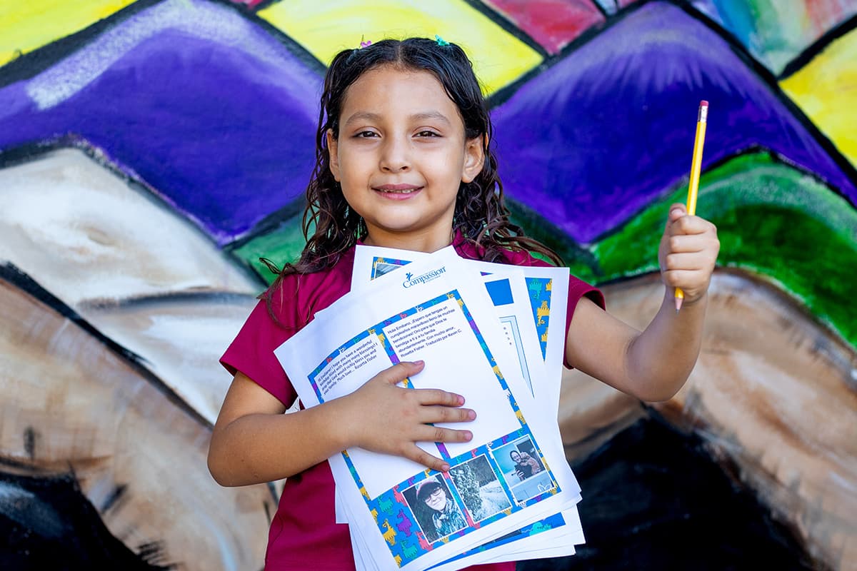 A young girl is smiling as she holds a pencil in the air.