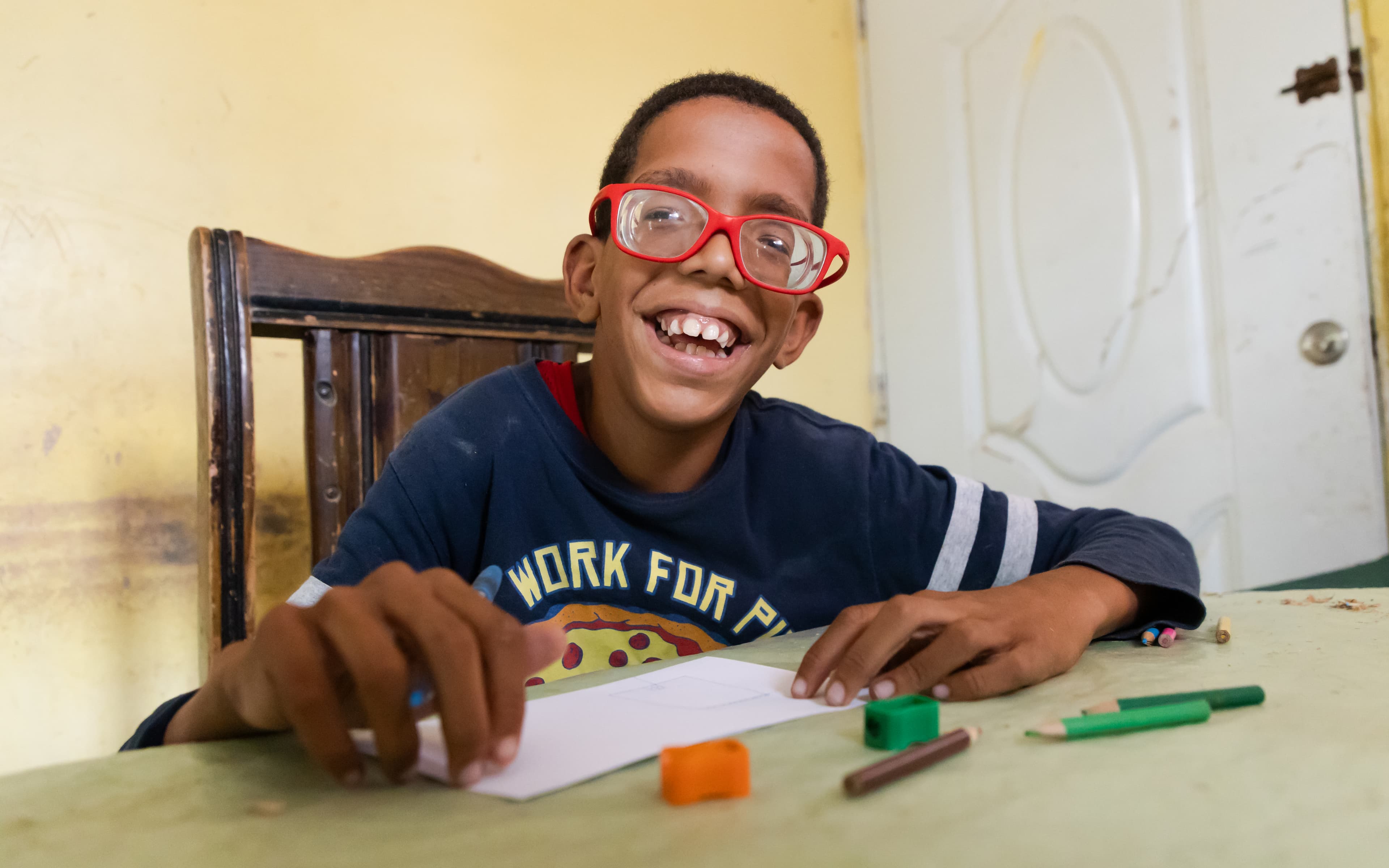 A young boy wearing bright red glasses smiles brightly for the camera.