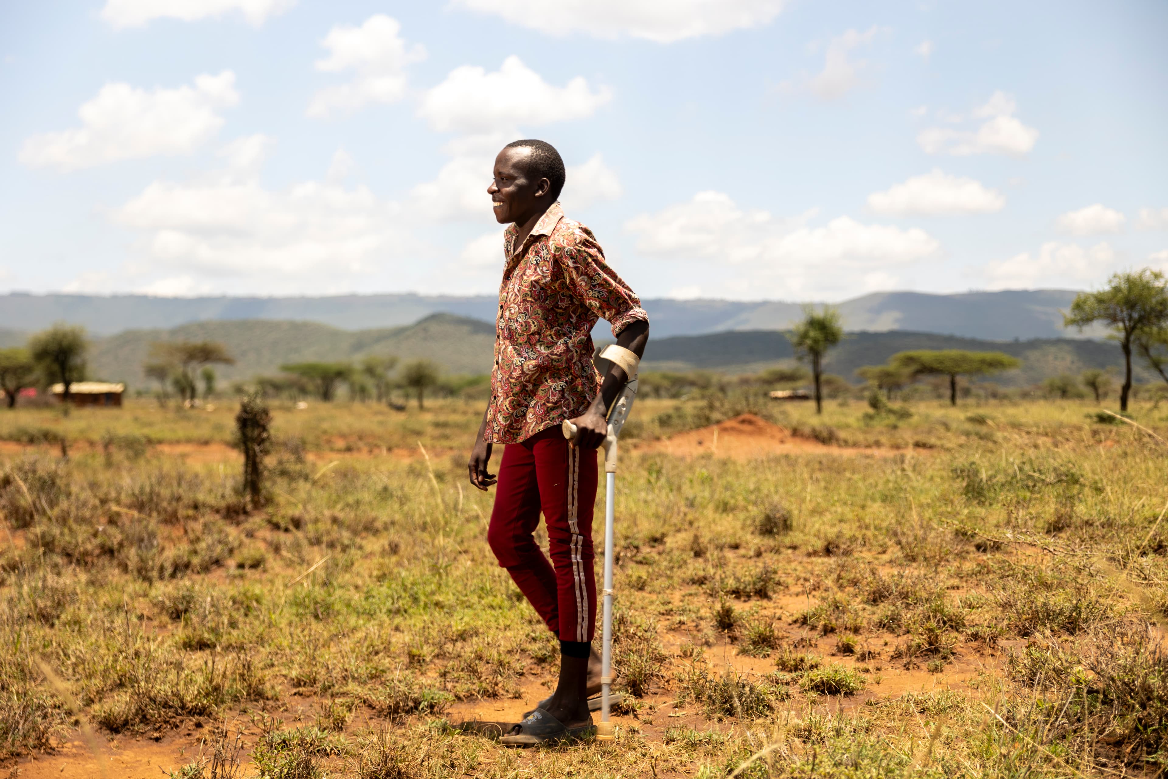 A young man is standing in a field holding a crutch that helps him walk.