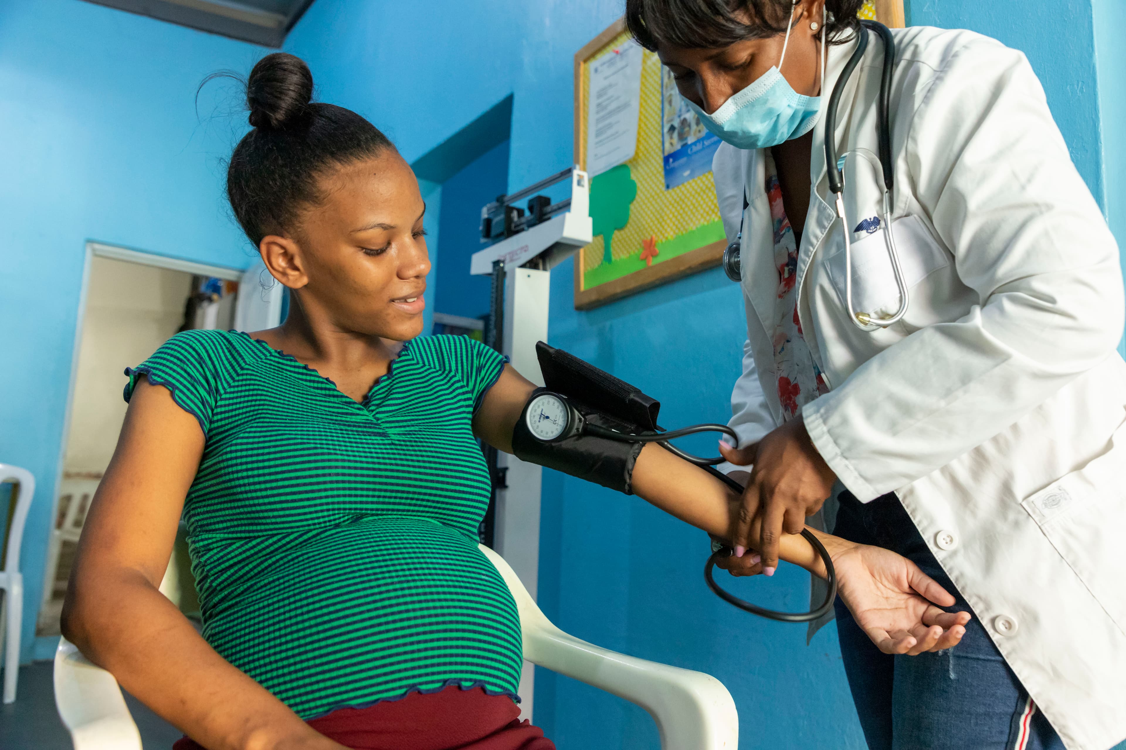 A pregnant mother sits in a chair as a doctor takes her blood pressure.