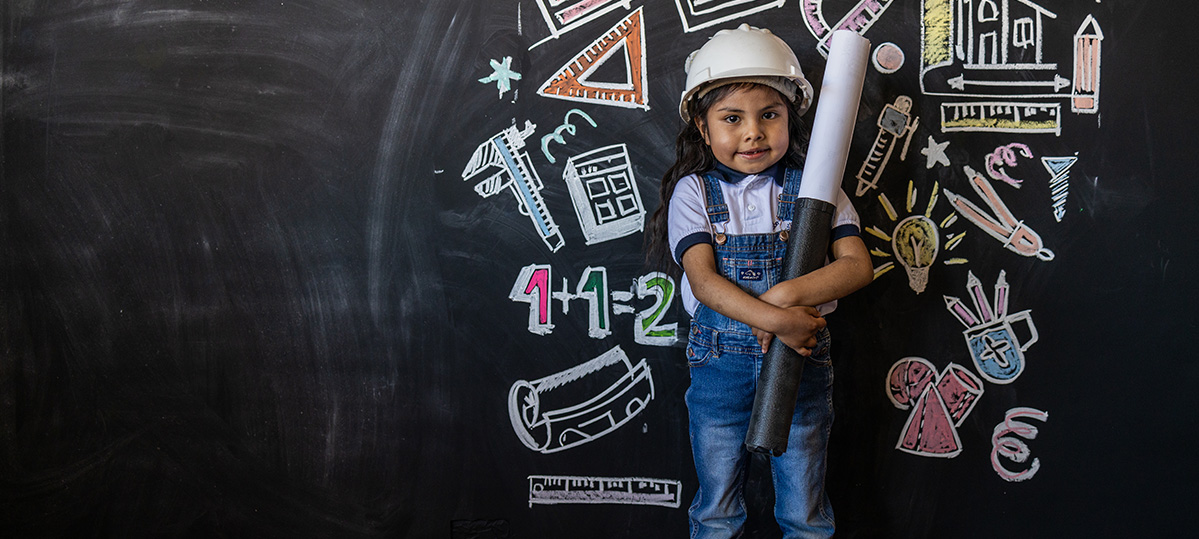 young girl dressed as a contractor stands in front of a chalkboard