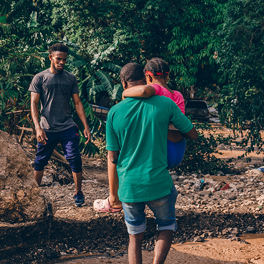 a young girl is carried across a river after Hurricane Meslissa